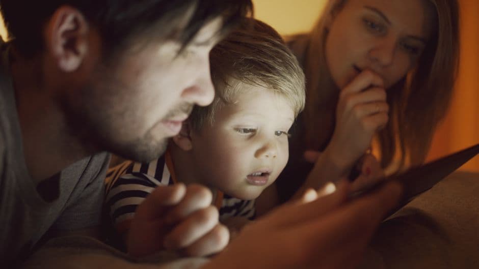 A family of three, including parents and a child, intently watching a digital tablet together indoors.