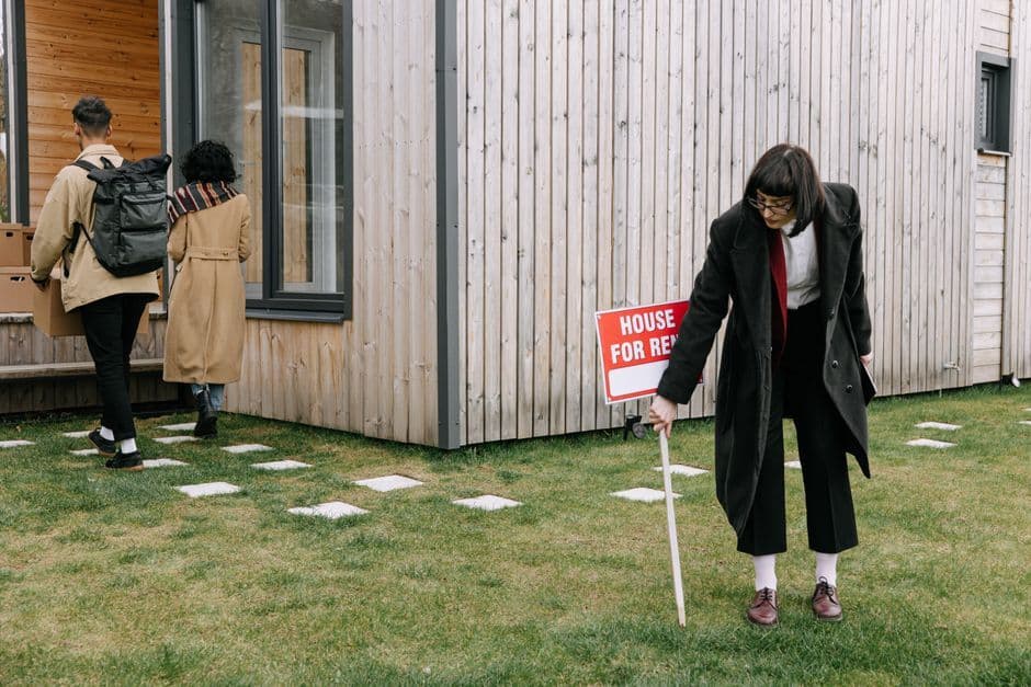 A couple moving into a new rental house as a real estate agent places a sign outside.